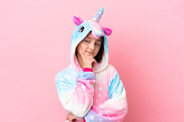 Little caucasian woman wearing a unicorn pajama isolated on pink background thinking an idea while...