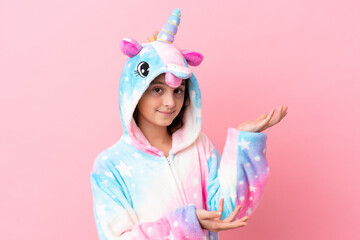 Little caucasian woman wearing a unicorn pajama isolated on pink background extending hands to the side for inviting to come