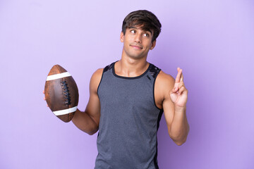 Young man playing rugby isolated on purple background with fingers crossing and wishing the best