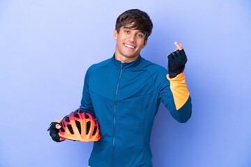 Young cyclist caucasian man isolated on purple background making money gesture