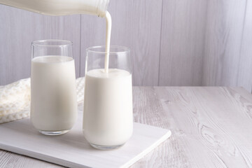 Pouring homemade kefir, buttermilk or yogurt with probiotics. Yogurt flowing from glass bottle on light background. Probiotic cold fermented dairy drink. Trendy food and drink. Copy space