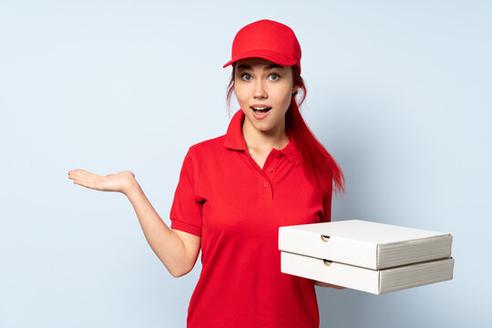 Pizza delivery girl holding a pizza over isolated background with shocked facial expression