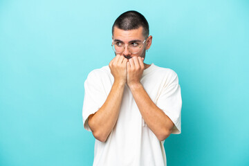 Young caucasian man isolated on blue background nervous and scared putting hands to mouth