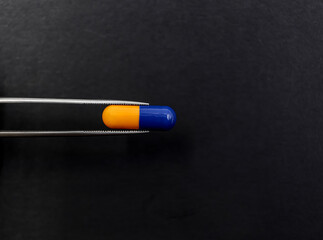 Pliers holding a pill of analgesic or anti-inflammatory for the gut on black background