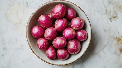 Overhead shot of a bowl filled with small, round, red potatoes, set against a marble background.