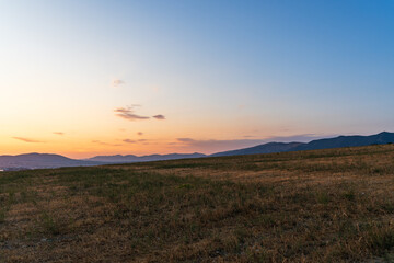 Sunset over a dry grassy field with distant mountain range under a clear gradient sky.