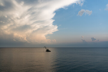 A lone crane barge floats on the calm sea under a dramatic evening sky with layered clouds