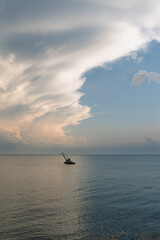 A lone crane barge floats on the calm sea under a dramatic evening sky with layered clouds
