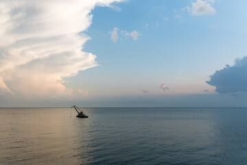 A lone crane barge floats on the calm sea under a dramatic evening sky with layered clouds