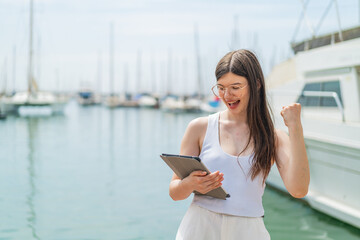 Young pretty Ukrainian woman holding a tablet at outdoors celebrating a victory