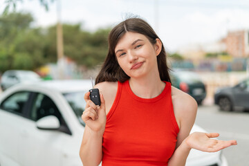 Young pretty Ukrainian woman holding car keys at outdoors making doubts gesture while lifting the...