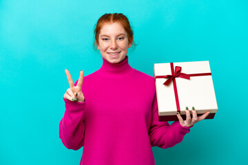 Young caucasian reddish woman holding a gift isolated on blue background smiling and showing...