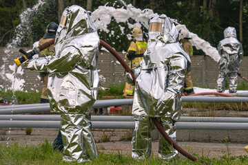 Firefighters in protective clothing use fire fighting equipment to supply water to extinguish the...