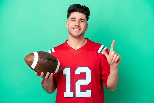 Young caucasian man playing rugby isolated on green background showing and lifting a finger in sign of the best