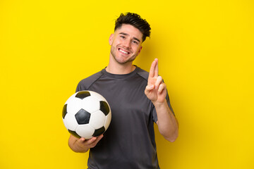 Handsome young football player man isolated on yellow background with fingers crossing and wishing...