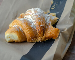 A bitten fresh croissant closeup on a craft paper.