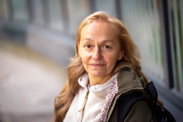 Old cheerful woman with a smiiley face walks in the city in the autumn sunny day.