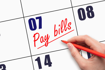 7th day of the month.  Hand writing Pay bills reminder and drawing a line on calendar with red pen...
