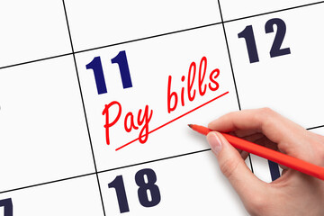 11th day of the month.  Hand writing Pay bills reminder and drawing a line on calendar with red pen...