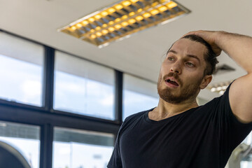Young attractive fitness trainer feels exhausted and thirsty after too much exercise on a treadmill. A sport man gets dehydrated from treadmill running over long period of time in a fitness room