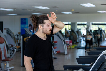 Young attractive fitness trainer feels exhausted and thirsty after too much exercise on a treadmill. A sport man gets dehydrated from treadmill running over long period of time in a fitness room