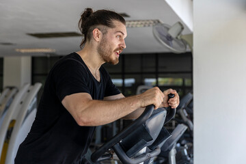 Attractive good looking fitness trainer shows how to use Elliptical Trainer to improve leg strength and building muscles in a gym. A sport man is running on a Elliptical Trainer to start his workout