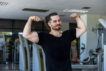 Smart good looking fitness trainer shows his muscle with confident after a workout program in a gym. A strong man expresses hit physical fit after achieving a long bodybuilding program