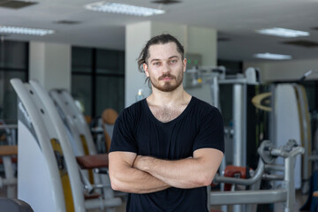 Smart good looking fitness trainer shows his muscle with confident after a workout program in a gym. A strong man expresses hit physical fit after achieving a long bodybuilding program