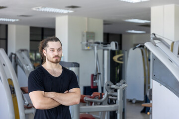 Smart good looking fitness trainer shows his muscle with confident after a workout program in a gym. A strong man expresses hit physical fit after achieving a long bodybuilding program