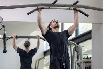Young good looking physical trainer shows how to build upper part body by pulling up an equipment in a fitness room. A muscular sport man taking an exercise with fitness equipment to build his body.