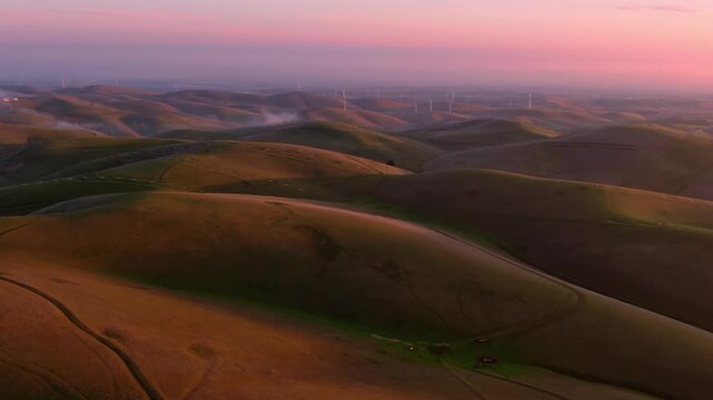 Rolling hills at sunrise in Altamont Pass, Livermore, California, USA. Wind turbines generate clean energy in the distance. The landscape shows the beauty of renewable energy.