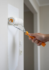 Male hand painting wall with white paint roller. Painting apartment, renovating concept