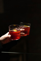 Hand Holding Red Cocktail with Citrus Peel and Ice Cube in front Mirror