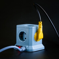 A modern blue cube-shaped power strip with a red illuminated switch, featuring multiple European...