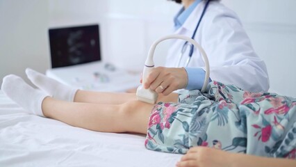 Doctor and kid patient. Orthopedist performing ultrasound examination on a child's knee in...