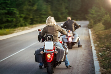 Rear view of two bikers riding on a scenic road through the forest at sunset. Mature couple on cruiser motorcycles enjoying freedom, nature, and the open road.