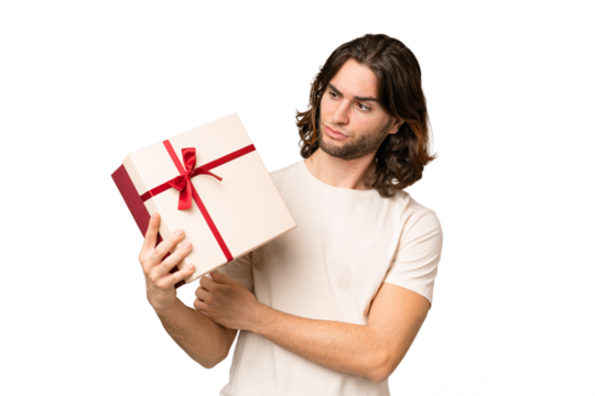 Young handsome man holding a gift over isolated background with sad expression