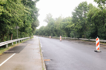 Road construction zone in forest area. Asphalt surface with traffic barriers. Wet street after...
