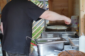  Street vendor prepares crepes on a hot griddle in an outdoor setting. The process involves...