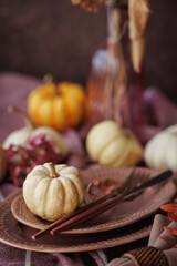 An elegant autumn table arrangement featuring white pumpkins, muted pink dishware, and natural...