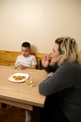 Mother and son drinking tea with pastries at the table in the kitchen.