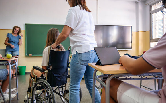 Teacher assisting a student in a wheelchair during inclusive classroom activity with tablets and diverse participation
