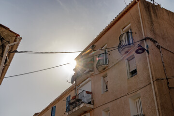 Balconies in sunlight with lens flare and wires, France, Corsica, Cargèse, 15 June 2025