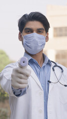Vertical Photo of Indian Doctor Checking Temperature with Thermometer Wearing Mask and Gloves