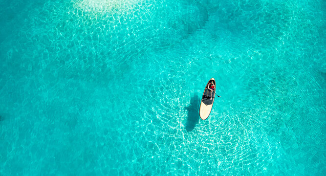 Fantastic aerial top view woman paddle boarding in crystal clear tropical sea bay summer outdoor activity water sport recreation turquoise ocean adventure travel destination scenic nature wallpaper - Powered by Adobe