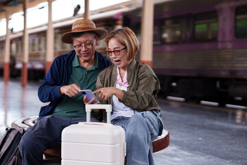 Older Asian couple enjoy train station travel planning using smartphone technology
