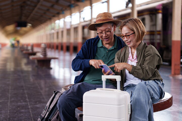 Older Asian Couple Using Smartphone Sitting Train Station Planning Journey Travel Destination Happy...