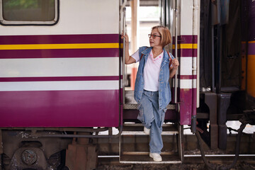 Older Asian female tourist travel journey railway station platform stepping train transit senior...