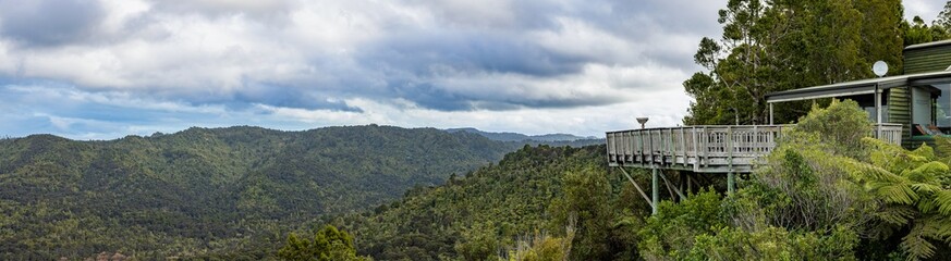 A panoramic view of the Waitakere Ranges from a wooden deck in Auckland, New Zealand. The deck is...