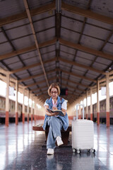 Older Asian Woman Tourist Sits Train Station Bench Writing Planning Solo Travel Journey Retirement Adventure Leisure Transit Hub Vacation